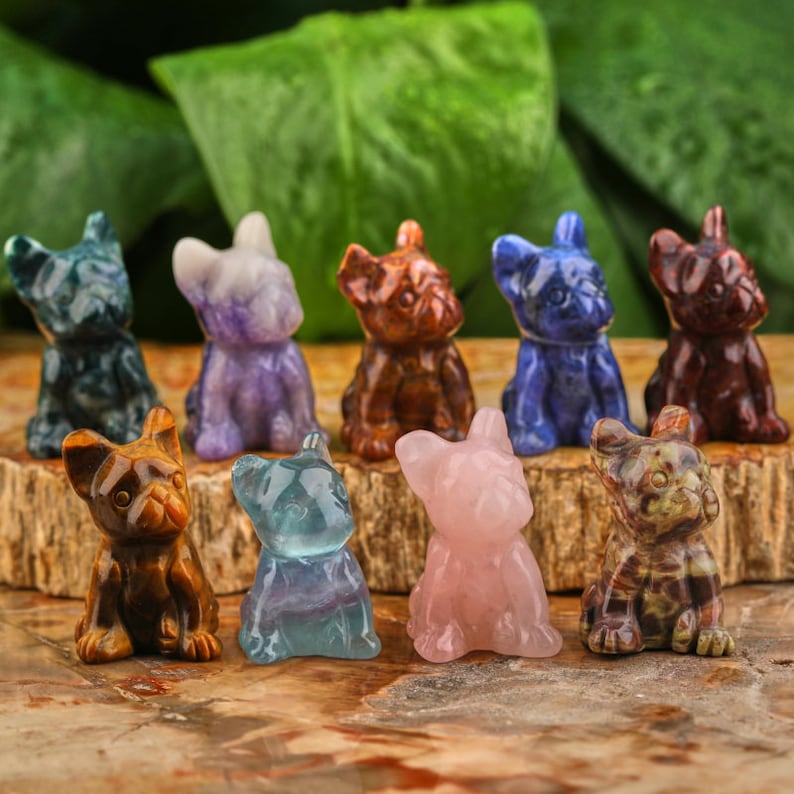 May include: A collection of ten small, hand-carved crystal dog figurines. The figurines are in various colors, including blue, green, pink, brown, and purple. They are all in the same pose, sitting with their heads tilted slightly to the side.