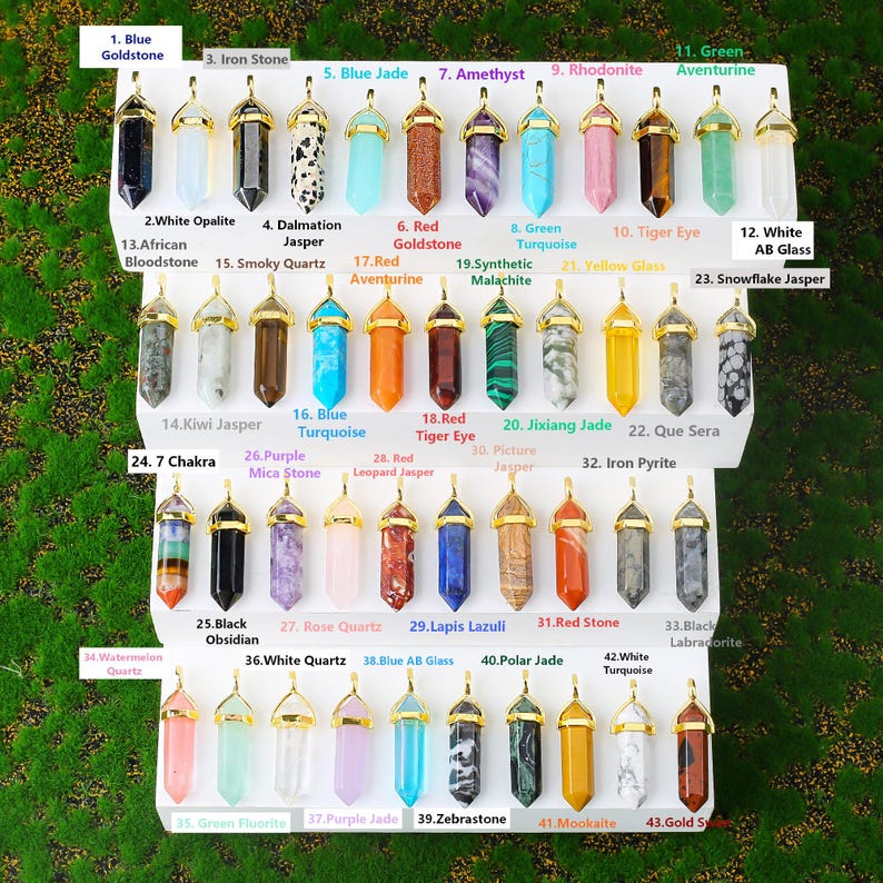 Puede incluir: Una colecci&oacute;n de colgantes de piedras preciosas en varios colores, incluyendo azul, morado y verde. Cada colgante tiene una tapa dorada y est&aacute; etiquetado con su tipo de piedra preciosa, como "Amatista" y "Cuarzo Rosa".