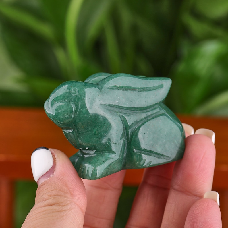 May include: A green jade rabbit figurine. The rabbit is carved in a sitting position with its ears raised.
