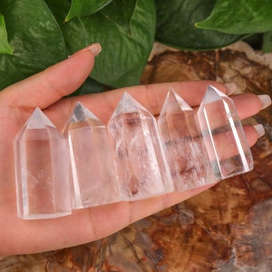 Puede incluir: Seis puntas de cristal de cuarzo transparente, también conocidas como varitas, están dispuestas en una fila sobre una mano. Las puntas son todas aproximadamente del mismo tamaño y forma, y tienen un acabado liso y pulido.