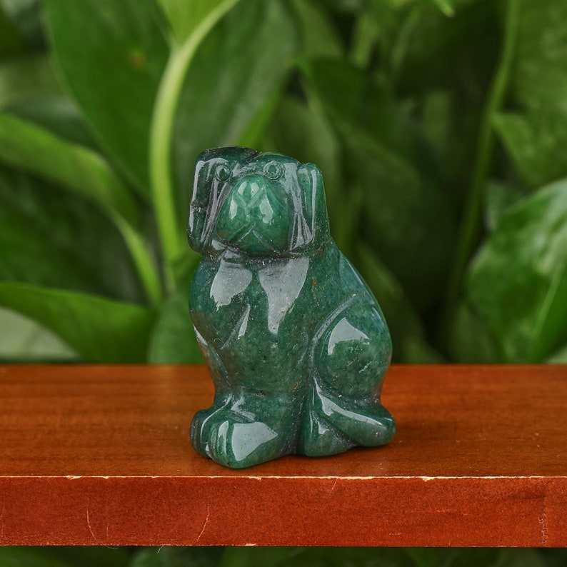 May include: Green jade stone carving of a dog sitting with its head tilted up. The carving is detailed and realistic, with a smooth, polished finish.