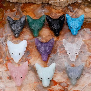 May include: Twelve carved wolf head pendants made of various semi-precious stones. The pendants are in shades of grey, green, black, blue, white, purple, pink, and light blue.