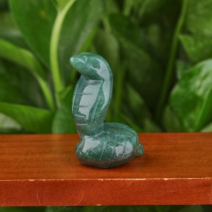 May include: Green jade stone carving of a cobra in a curled up position. The carving is detailed and realistic, with scales and eyes.