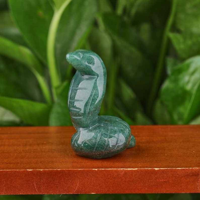 May include: Green jade stone carving of a cobra in a curled up position. The carving is detailed and realistic, with scales and eyes.