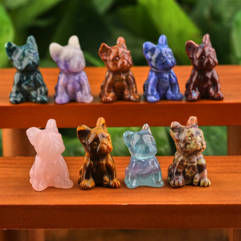 May include: A collection of eight small, carved, crystal dog figurines. The figurines are in various colors, including green, purple, brown, blue, pink, tiger's eye, blue fluorite, and brown and white.