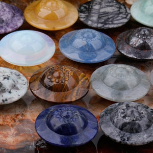 May include: A collection of 10 small, round, polished stone coasters in various colors and patterns. The coasters are shaped like flying saucers and have a raised center.