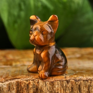 May include: A small, brown and gold tiger's eye crystal carved into the shape of a sitting dog. The dog has a shiny, polished finish.