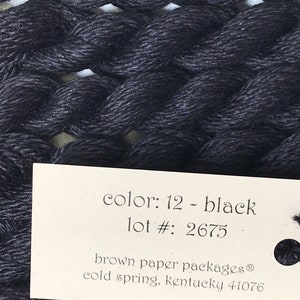May include: Close-up of a skein of black embroidery floss. The label reads "color: 12 - black" and "lot #: 2675". The floss is tightly wound, showing the texture of the thread. The label also includes the brand and location.