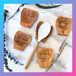 Puede incluir: Cuatro reposacucharas de madera con el texto "in the [name] kitchen we dance" grabado en cada uno. Los reposacucharas están sobre una superficie blanca con una cuchara de madera en el centro.