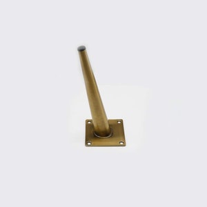 May include: A gold metal furniture leg with a square base and a tapered design. The leg is approximately 6 inches tall.