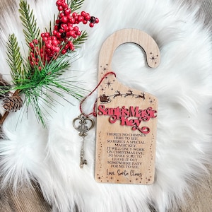 May include: A wooden door hanger with a red and white Santa's Magic Key design. The hanger has a keyhole and a string with a small key attached. The text on the hanger reads: "There's no chimney here to see, so here's a special magic key. It will only work on Christmas Eve, so make sure to leave it out somewhere easy for me to see. Love, Santa Claus."