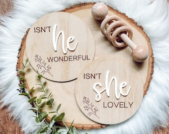 May include: Two wooden signs with the text "Isn't he wonderful" and "Isn't she lovely" with a small wooden rattle on a wooden surface.