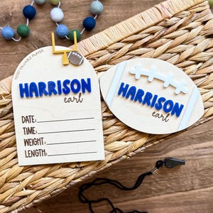 May include: Two wooden football-themed name plaques. One is shaped like a football field goal, the other a football. Both have the name "HARRISON" in blue, with "earl" in script. The field goal plaque has lines for date, time, weight, and length.