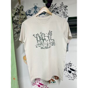 May include: A cream-colored t-shirt with a green graphic of three frogs dancing and the text "Frolicking..." printed on the front.