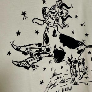 May include: Black and white illustration of a cow wearing a cowboy hat and boots, with stars and the text "Yee Haw" on a white background.