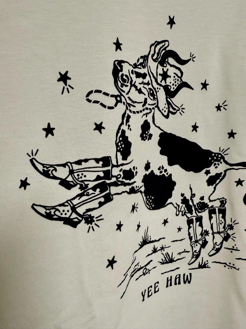 May include: Black and white illustration of a cow wearing a cowboy hat and boots, with stars and the text "Yee Haw" on a white background.