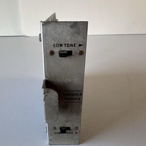 May include: A rectangular silver-colored metal electronic encoder module with a weathered finish. The front panel features black text reading LOW TONE and HIGH TONE, each with a small black sliding switch and a directional arrow indicator.