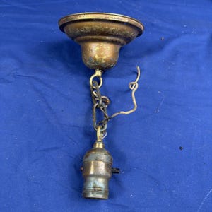 May include: A vintage brass ceiling light fixture canopy with a weathered patina, featuring a circular mounting plate, a short metal chain link suspension, and a single light bulb socket with a small black turn-knob switch and exposed wiring.