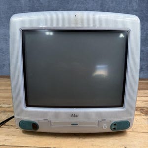 Puede incluir: Un ordenador de sobremesa iMac G3 vintage de color blanco y gris translúcido con un patrón de rayas en la carcasa, un monitor de tubo de rayos catódicos, altavoces integrados, una unidad de disco óptico frontal y un botón de encendido.