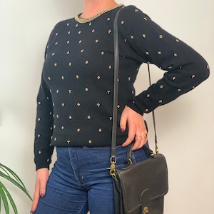 May include: A black sweater with gold sequins and a black leather shoulder bag.