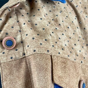 May include: Close-up of a brown suede jacket with black polka dots and a blue denim collar. The jacket has two large buttons on the front, one of which is visible in the image.
