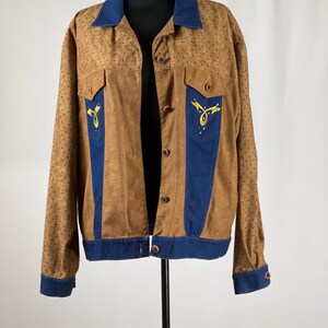May include: A brown suede jacket with blue denim accents and gold embroidery. The jacket has a button-up front and long sleeves.