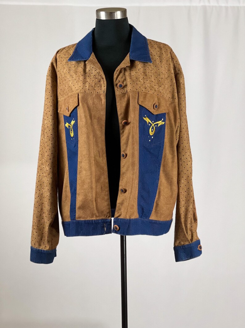 May include: A brown suede jacket with blue denim accents and gold embroidery. The jacket has a button-up front and long sleeves.