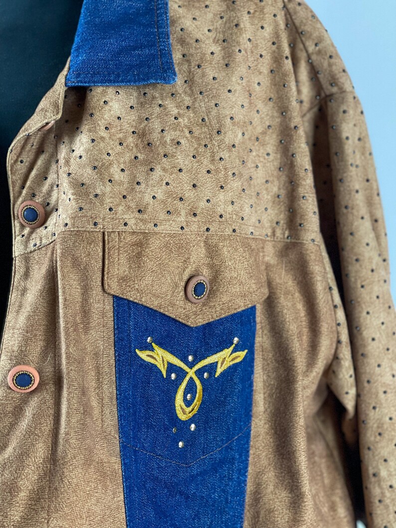 May include: A brown suede jacket with a blue denim collar and a blue denim pocket with gold embroidery. The jacket has a pattern of small black dots.