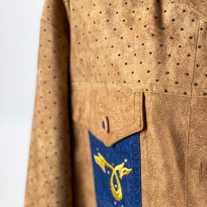 May include: A brown suede jacket with a blue denim collar and a blue denim panel on the front. The jacket has a gold embroidered design on the denim panel.