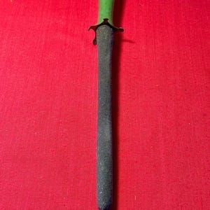 May include: A sharpening steel featuring a textured, dark gray cylindrical rod and a smooth, bright green handle. A small, dark metal guard separates the handle from the rod, providing a clear distinction between the two functional sections.