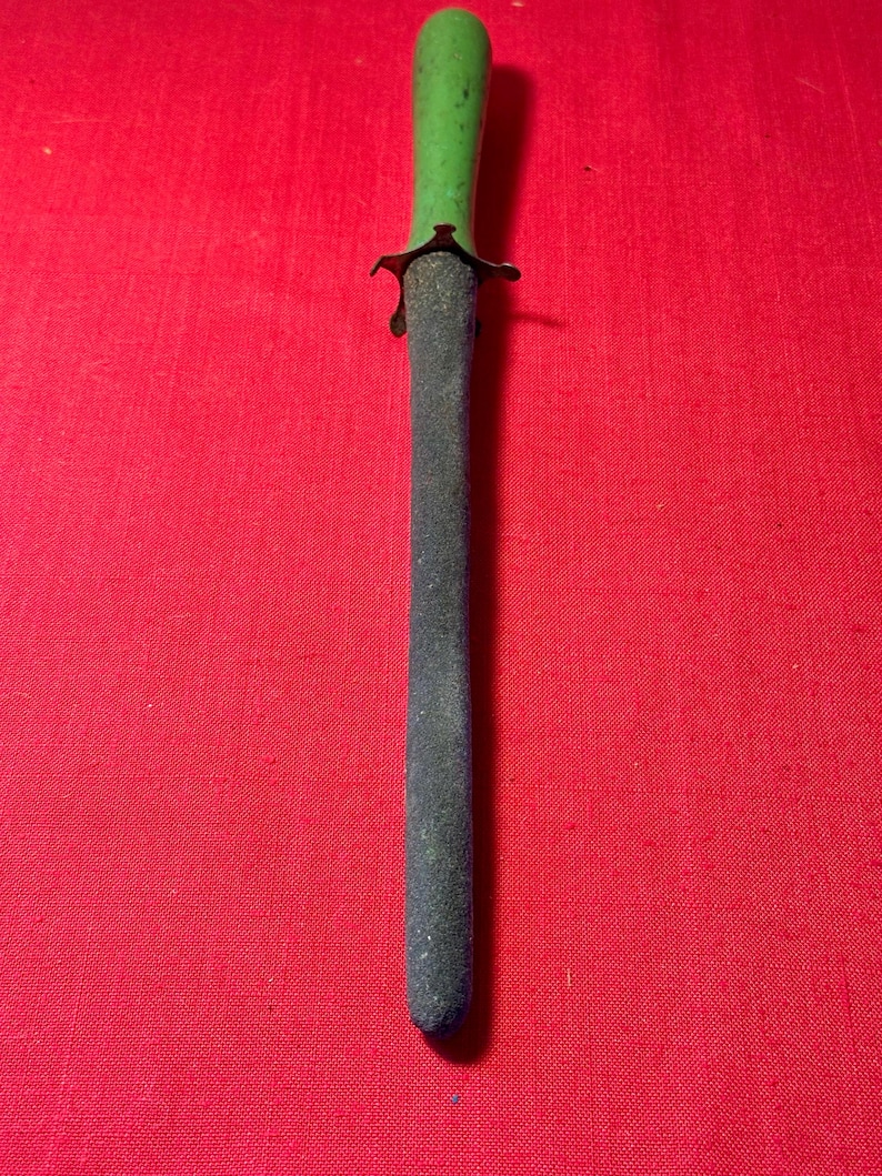 May include: A sharpening steel featuring a textured, dark gray cylindrical rod and a smooth, bright green handle. A small, dark metal guard separates the handle from the rod, providing a clear distinction between the two functional sections.