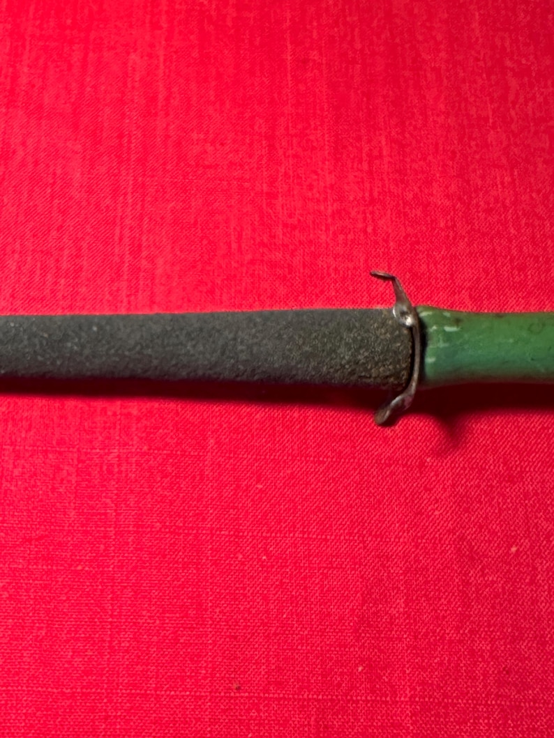 May include: A sharpening tool featuring a dark gray, textured, conical abrasive rod attached to a smooth, green-painted handle. A small, silver-colored metal guard separates the abrasive sharpening section from the handle of the tool.