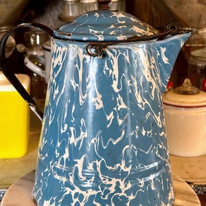 May include: A blue and white marbled enamel pitcher with a black handle and a lid. The pitcher has a rustic, vintage look.