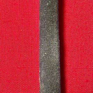May include: A long, narrow, dark gray strip with a textured, granular surface. The strip is positioned vertically against a bright red background that features a fine, woven, cross-hatched fabric pattern throughout the entire visible area.