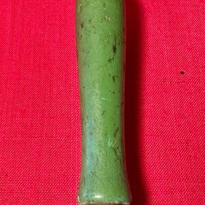 May include: A cylindrical handle with a smooth, light green painted finish showing signs of wear and dark scuff marks. The handle is attached to a metallic, multi-pronged base that connects to a dark, textured, cylindrical body below it.