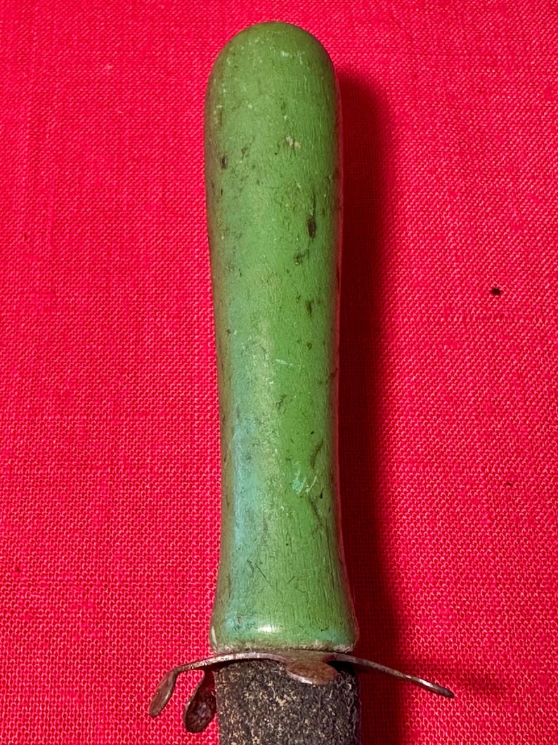 May include: A cylindrical handle with a smooth, light green painted finish showing signs of wear and dark scuff marks. The handle is attached to a metallic, multi-pronged base that connects to a dark, textured, cylindrical body below it.