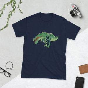 May include: Navy blue t-shirt featuring a green dinosaur graphic with red accents. The dinosaur design is stylized and cartoonish, with a detailed outline. The shirt is made of a soft material.