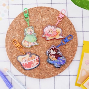 Könnte beinhalten: Vier farbenfrohe Schlüsselanhänger mit Cartoon-Shiba-Inu-Hunden in verschiedenen Kostümen. Die Schlüsselanhänger sind aus klarem Acryl gefertigt und haben eine glänzende Oberfläche. Die Hunde sind als Frosch, Blume, Meerjungfrau und Ramen-Schüssel verkleidet.