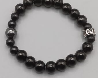 Op de afbeelding: Een zwart kralenarmband met een zilveren accent. De armband heeft ronde, glanzende zwarte kralen van verschillende maten. Een zilverkleurige spacer met een geometrisch ontwerp voegt details toe.