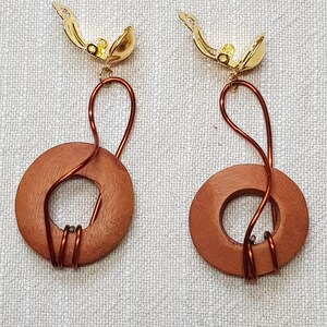 Könnte beinhalten: Ein Paar Ohrringe aus Holz mit einem goldenen Verschluss. Die Ohrringe bestehen aus zwei runden Holzstücken mit einem Loch in der Mitte. Das Holz ist dunkelbraun. Die Ohrringe sind durch einen dünnen Draht mit dem Verschluss verbunden.