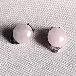 May include: A pair of clip-on earrings featuring round, pale pink gemstones. The earrings have a polished, glossy finish and are set on silver-colored metal clips. The background is a textured, light gray fabric.