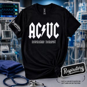 Könnte beinhalten: Ein schwarzes Kurzarm-T-Shirt mit weißem Aufdruck AC/VC, einem Blitz in der Mitte und dem Schriftzug RESPIRATORY THERAPIST darunter. Der rechte Ärmel zeigt das Wort Respiratory in weißer Schreibschrift, ein passender Aufnäher liegt bei.