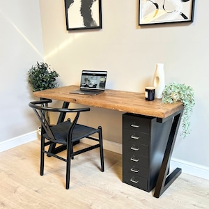 May include: A wooden desk with a black metal frame and a black six-drawer cabinet. A black chair sits in front of the desk, and a laptop is on the desk. Decorative items include a white vase, a candle, and a small plant.