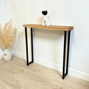 May include: A wooden console table with black metal legs. The table has a natural wood finish and is supported by two pairs of slender black metal legs.