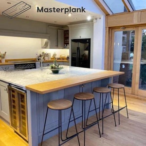May include: A kitchen island with a light grey countertop and a wooden top. Four black metal bar stools with wooden seats surround the island. The island has a built-in wine cooler and a light grey cabinet. The text "Masterplank" is visible on the ceiling.