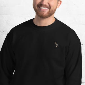 Pode incluir: Camisola de moletom preta com uma pequena imagem bordada de um &aacute;rbitro levantando o bra&ccedil;o no ar.
