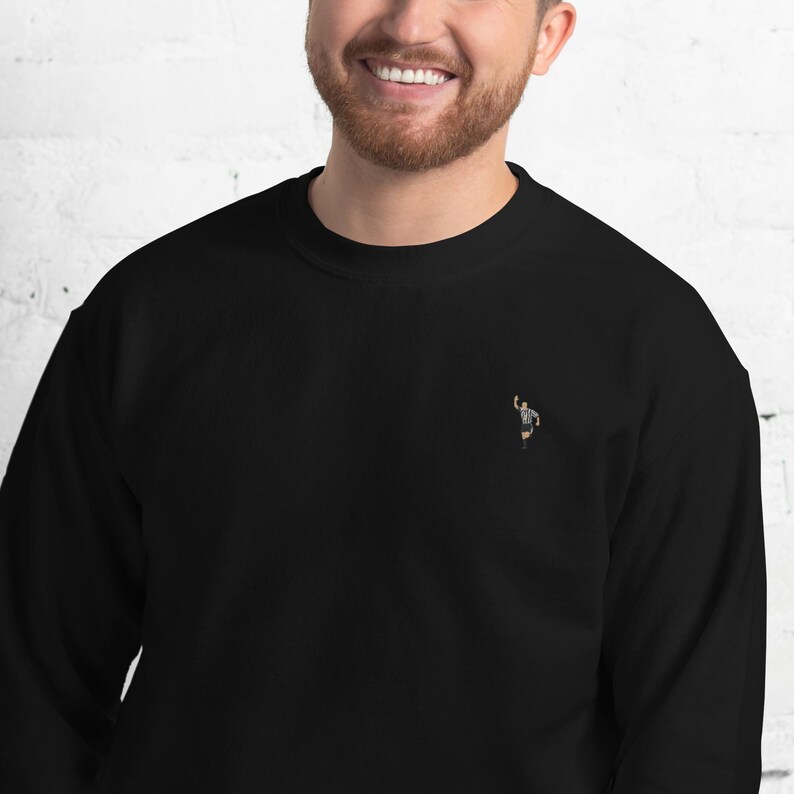 Pode incluir: Camisola de moletom preta com uma pequena imagem bordada de um &aacute;rbitro levantando o bra&ccedil;o no ar.