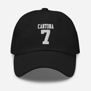 Puede incluir: Gorra de béisbol negra con el texto "CANTONA 7" bordado en blanco en la parte delantera.