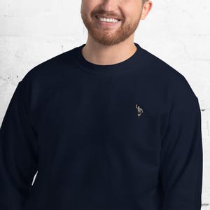 Pode incluir: Uma camisa de moletom azul marinho com uma pequena imagem bordada de uma pessoa em uniforme de &aacute;rbitro.