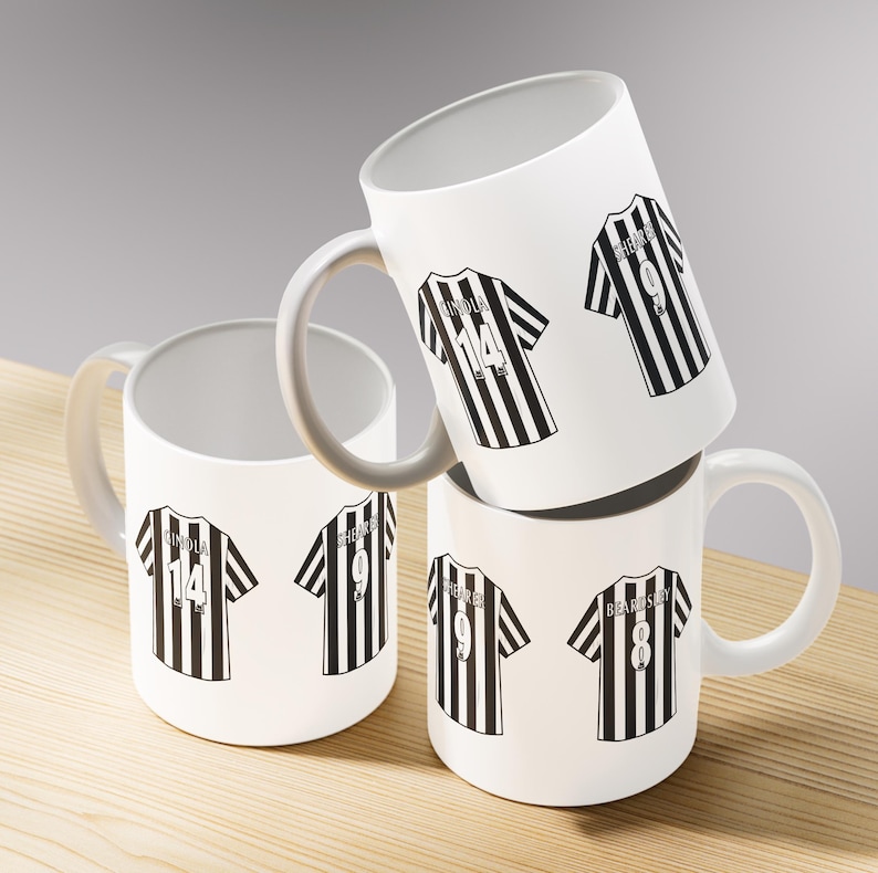 May include: Four white ceramic mugs with gray handles are stacked on a wooden surface. Each mug features a black and white striped jersey design with player names and numbers. The jerseys have the numbers 8, 9, and 14.